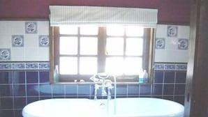 Un bagno con una vasca freestanding, una finestra con tenda e piastrelle decorative sulle pareti.