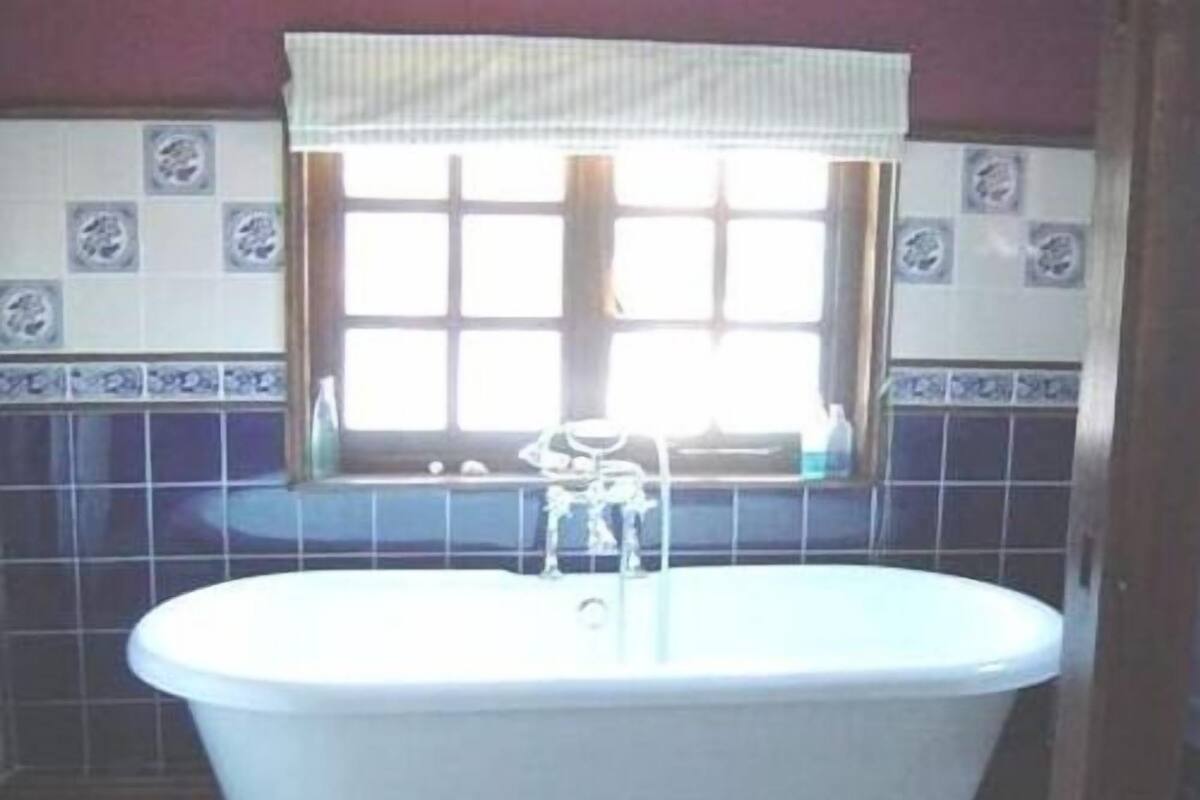 Een badkamer met een vrijstaand bad, een raam met gordijn en decoratieve tegels op de muren.