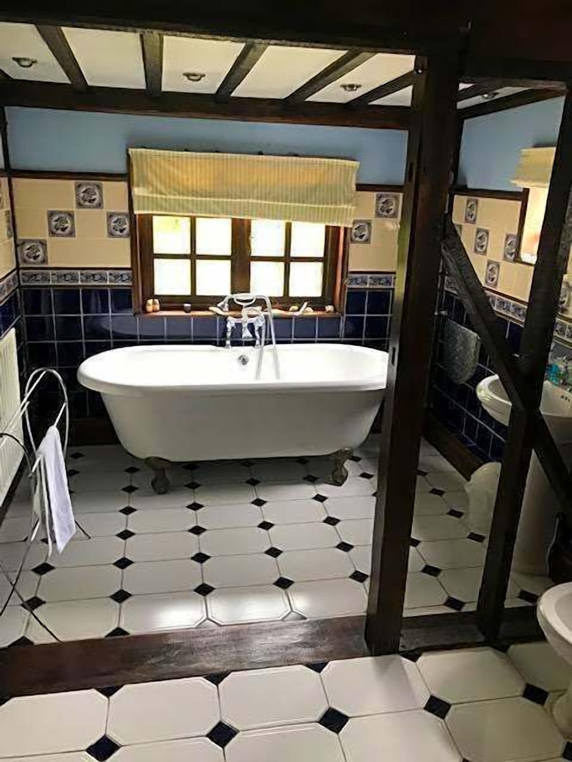 A bathroom with a freestanding bathtub, a window with a curtain, and a tiled floor.
