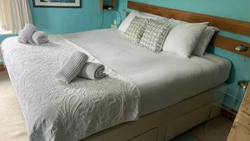 Una cama bien hecha con una colcha blanca y almohadas, un cabecero de madera y una mesita de noche con una lámpara.