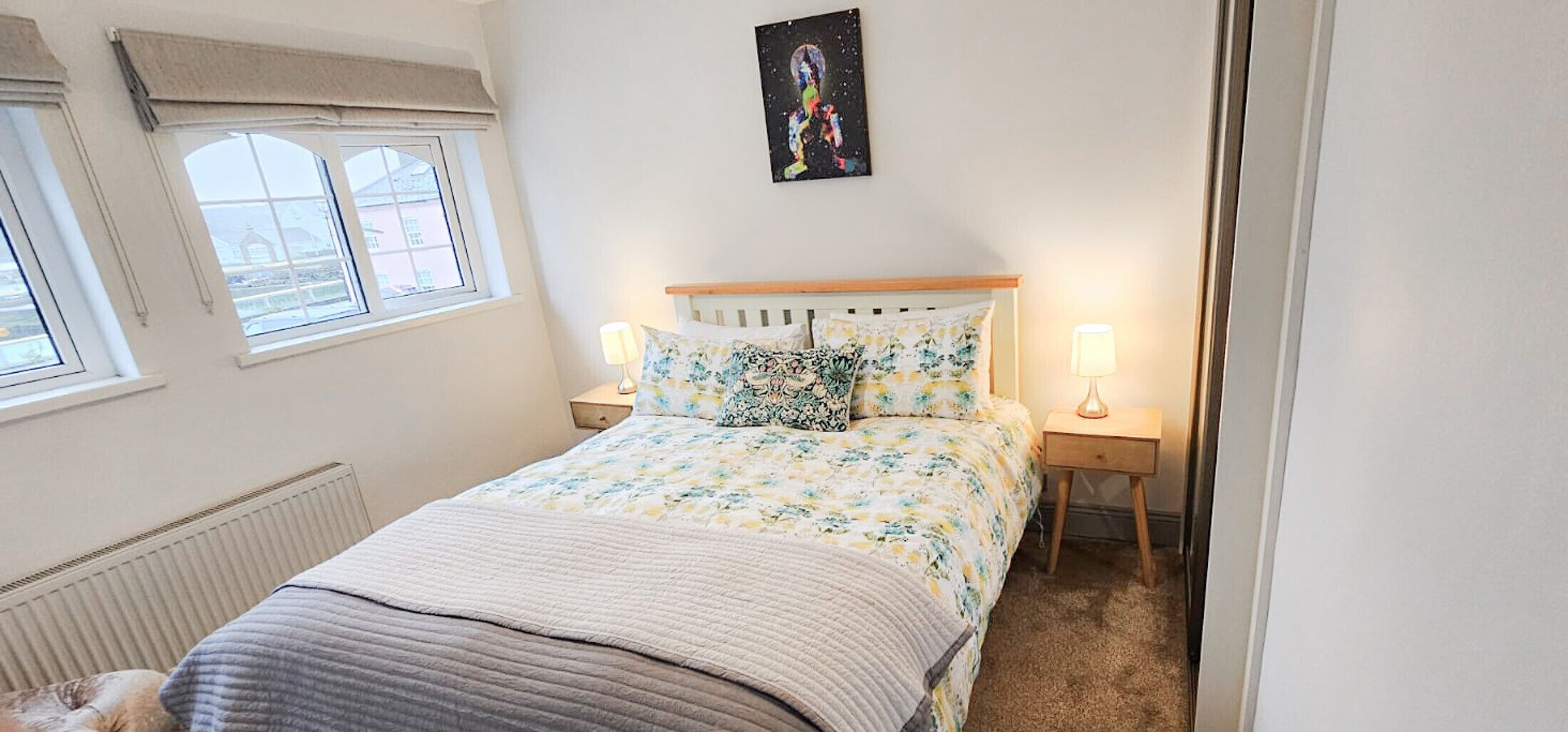 Un dormitorio con una cama, dos mesitas de noche, un ventanal y un cuadro en la pared.