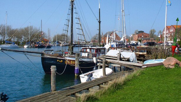 A marina with several boats docked, a wooden pier, and buildings in the background. - Apartment in Wenkendorf for 7 Personen (Fehmarn)