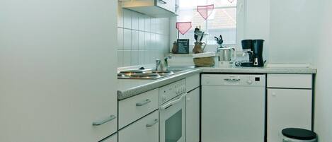 Cocina compacta con armarios blancos, lavavajillas, estufa y cafetera.