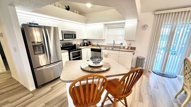 Una cocina moderna con armarios blancos, electrodomésticos de acero inoxidable y una isla central con sillas.