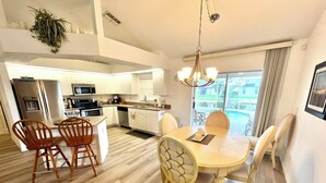 Una cocina moderna con armarios blancos, una isla central y una zona de comedor con una mesa redonda y sillas.