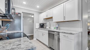 A modern kitchen with white cabinets, a stainless steel dishwasher, and a marble countertop.