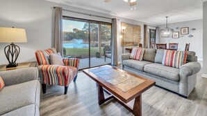 A spacious living room with a large window, a ceiling fan, and a dining area with chairs and a table.