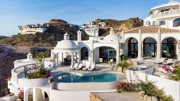 A luxurious villa with a swimming pool, outdoor seating, and a view of the surrounding landscape.