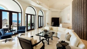A spacious living room with a large glass door leading to a balcony, a white sofa, a black coffee table, and a blue armchair.