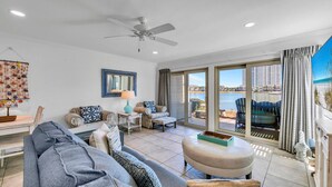 Ein geräumiges Wohnzimmer mit Deckenventilator, einem großen Fenster mit Blick auf den Strand und einem Essbereich mit Tisch und Stühlen.