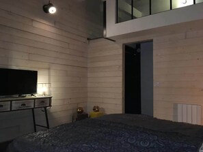 A bedroom with a bed, a TV on a dresser, and a door leading to another room.