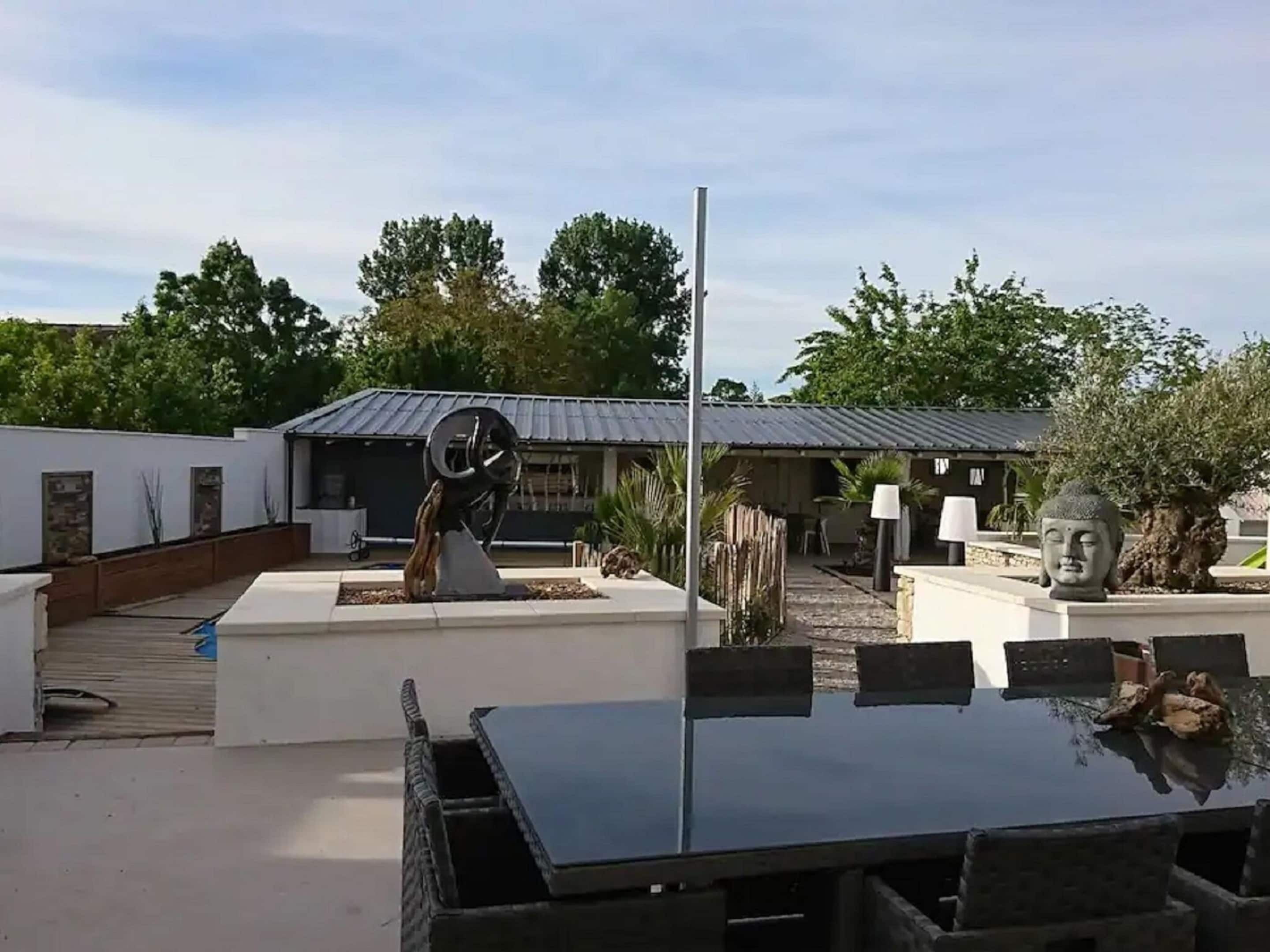 Ein moderner Essbereich im Freien mit einem Tisch und Stühlen, umgeben von einer weißen Mauer und einem Metallzaun.
