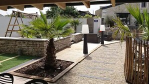 Ein Patio im Freien mit einer Holzpergola, Palmen und einer Steinmauer.