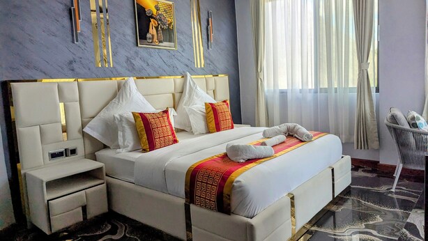 A modern hotel room with a large bed, a nightstand, a bedside table, and a window with sheer curtains. - twalumba resort and hotels (Lusaka)