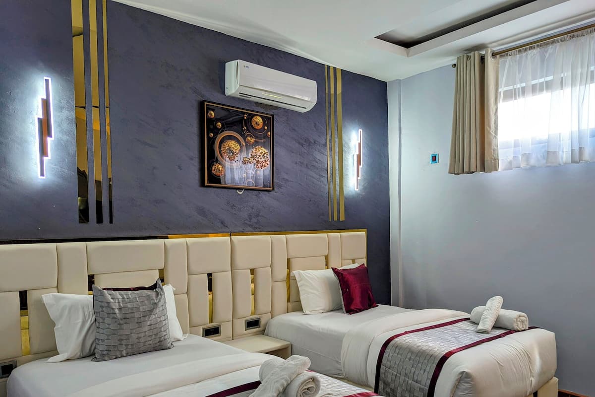 A hotel room with two beds, a modern air conditioning unit, a decorative wall piece, and a window with curtains.
