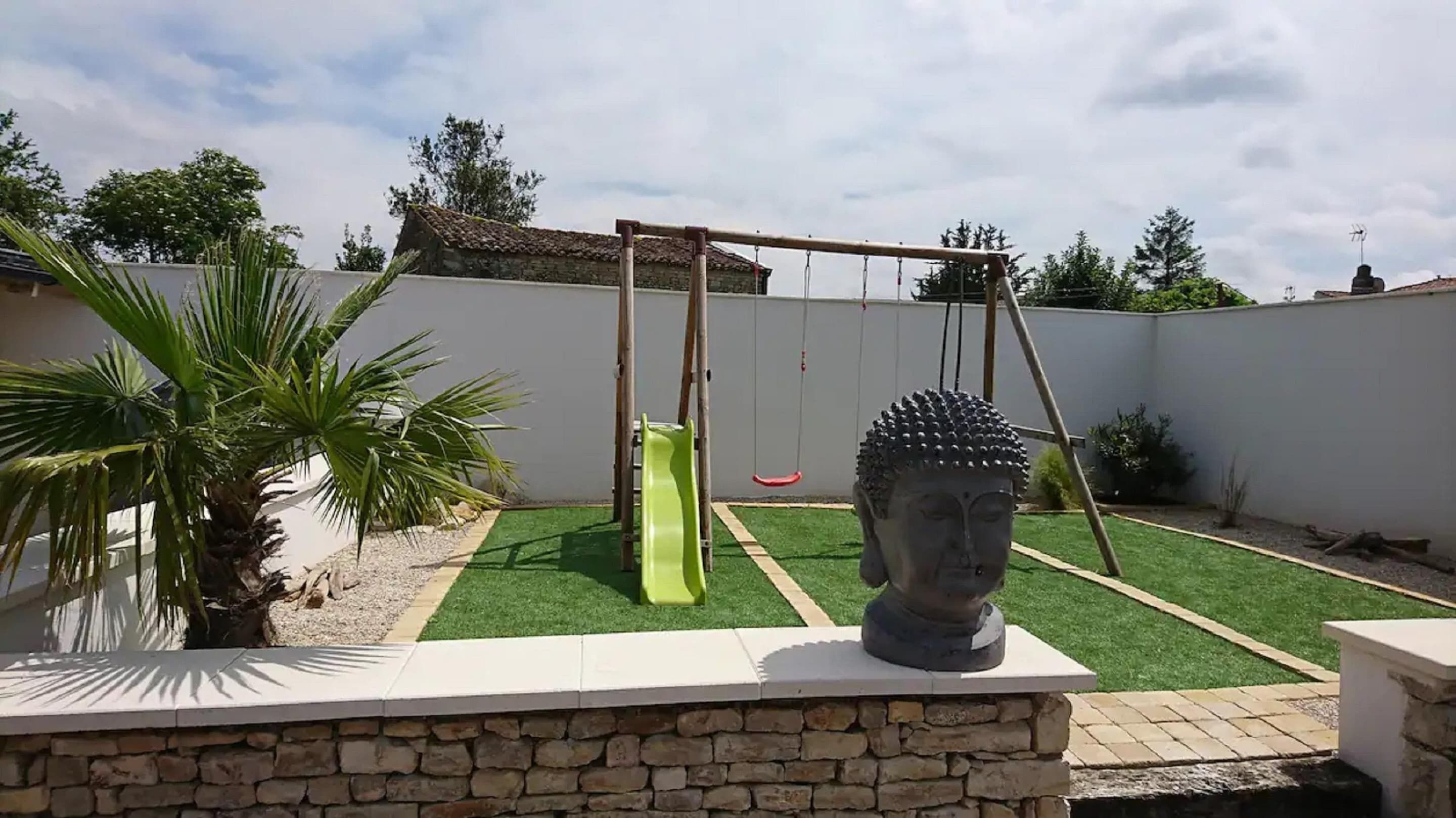 Een tuin met een schommel, een Boeddhabeeld en een palmboom.