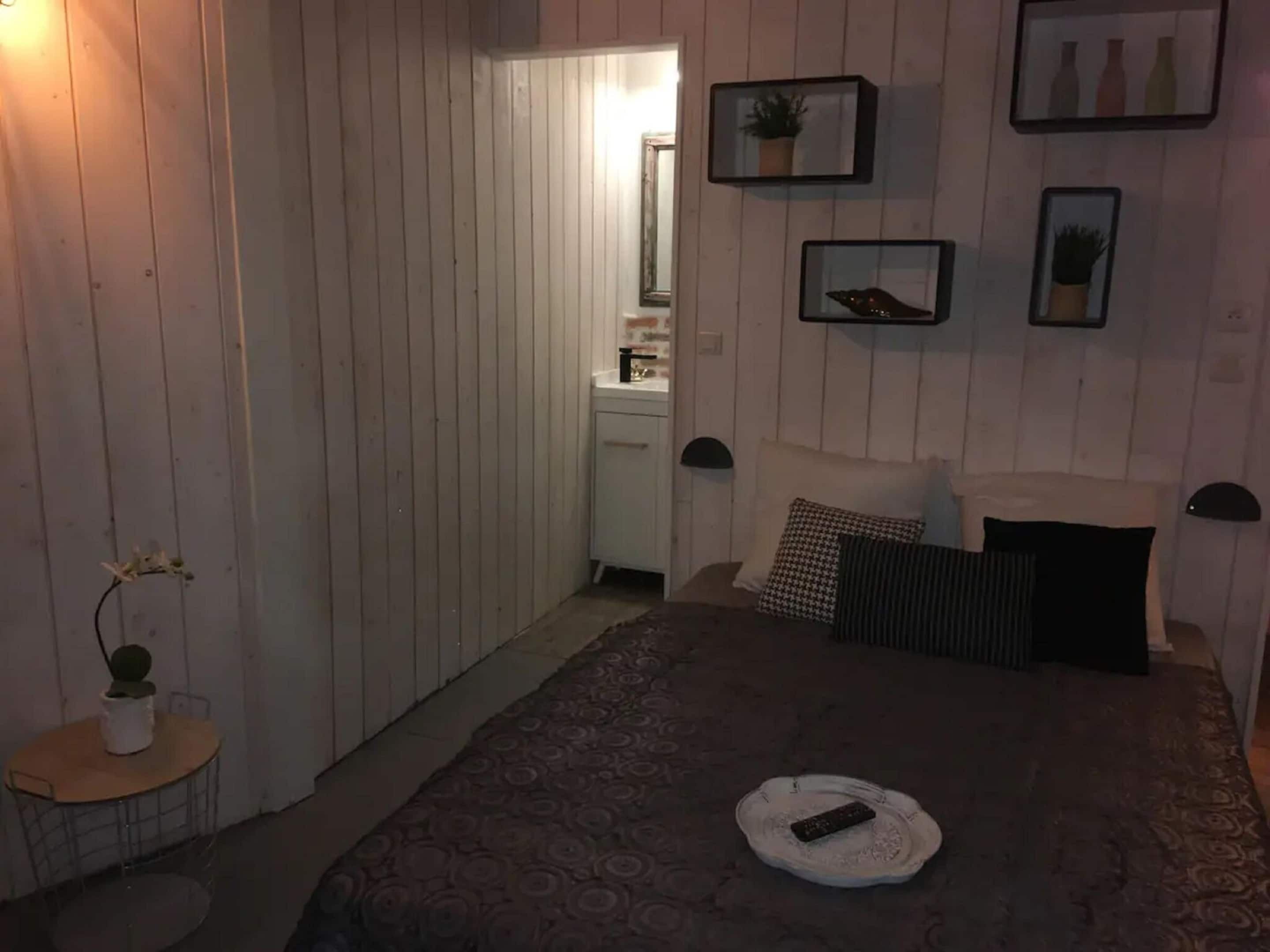 A bedroom with a bed, a bedside table, a small round table with a plant, and a door leading to a bathroom.
