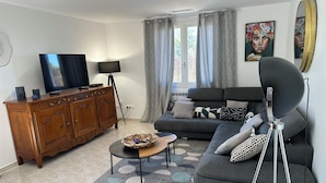 A modern living room with a sofa, a TV, a wooden cabinet, and a floor lamp. - Villa with Private Pool – Grau d’Agde – 6–8 Guests – Beach – AC (Agde)
