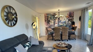 A modern living room with a sofa, a round coffee table, a dining area with wicker chairs, and a large abstract painting on the wall. - Villa with Private Pool – Grau d’Agde – 6–8 Guests – Beach – AC (Agde)
