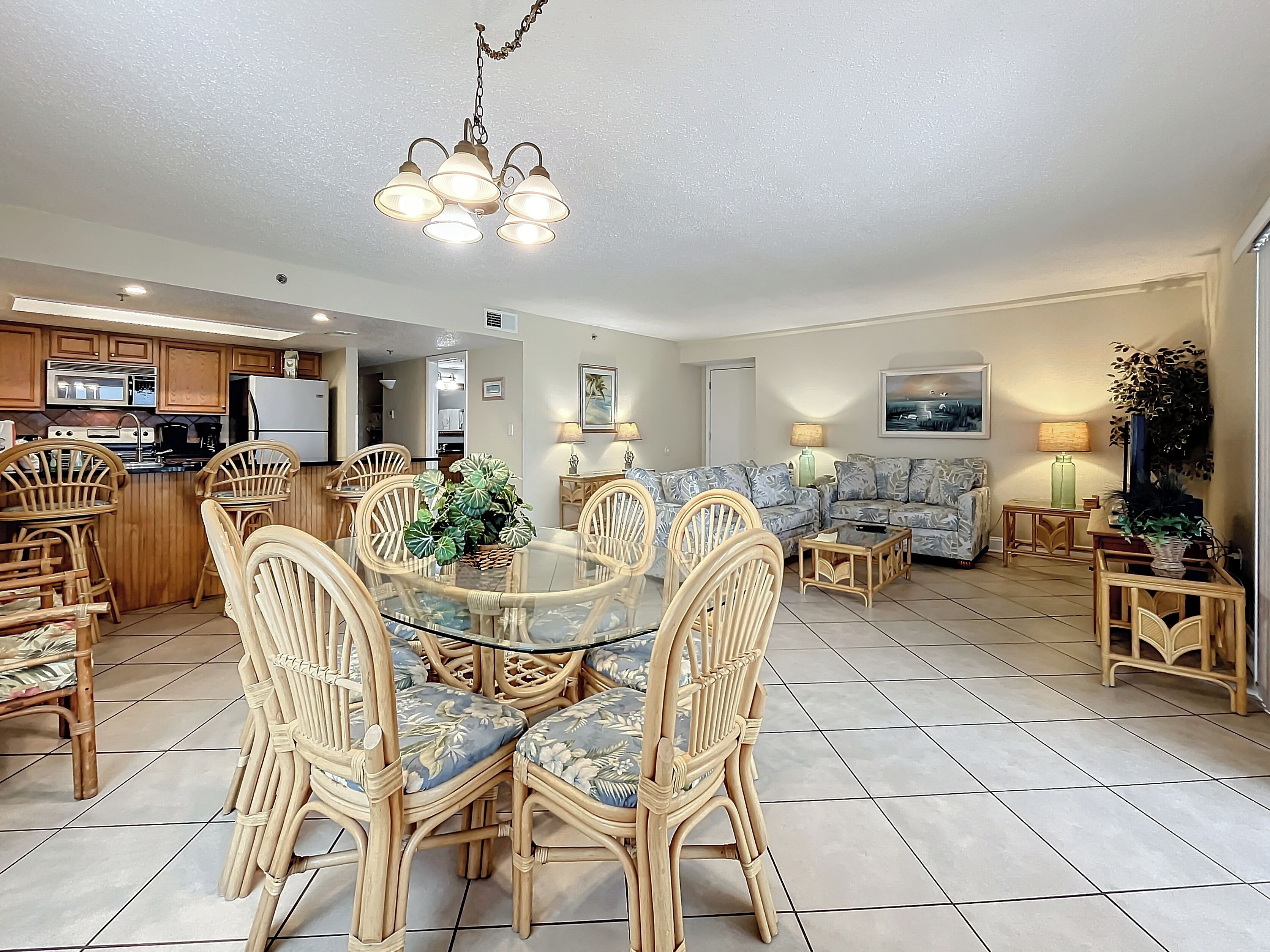 A spacious living area with a glass dining table surrounded by wicker chairs, a sofa, and a coffee table.