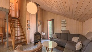 Un accogliente interno di una baita con arredamento in legno, un camino, un divano, un tavolo e una scala.