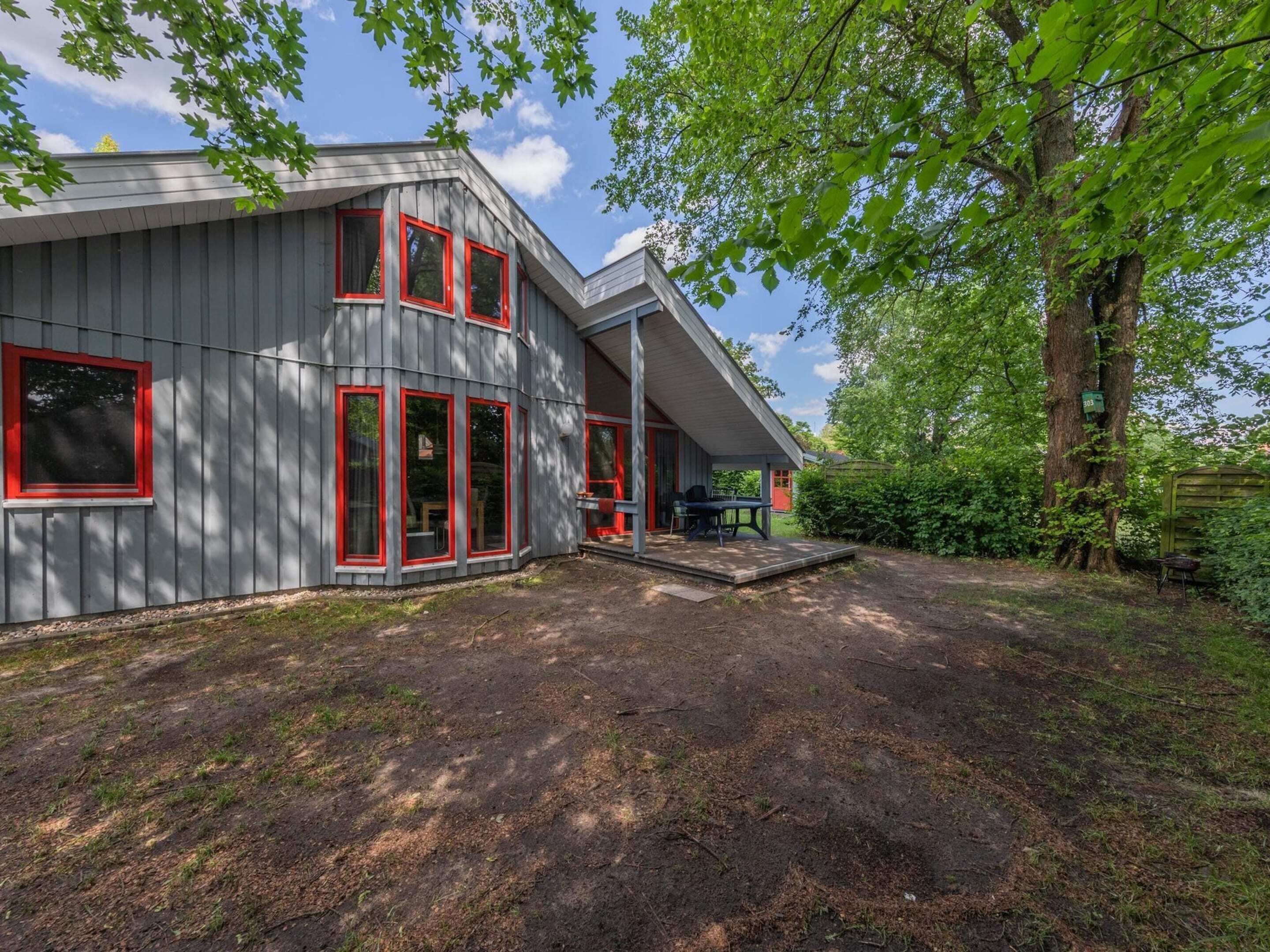 Een woonhuis met twee verdiepingen, een grijze gevel en rode raamkozijnen.