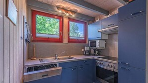 Una cucina compatta con lavastoviglie, fornello e microonde. Due finestre con cornici rosse e un soffitto in legno.