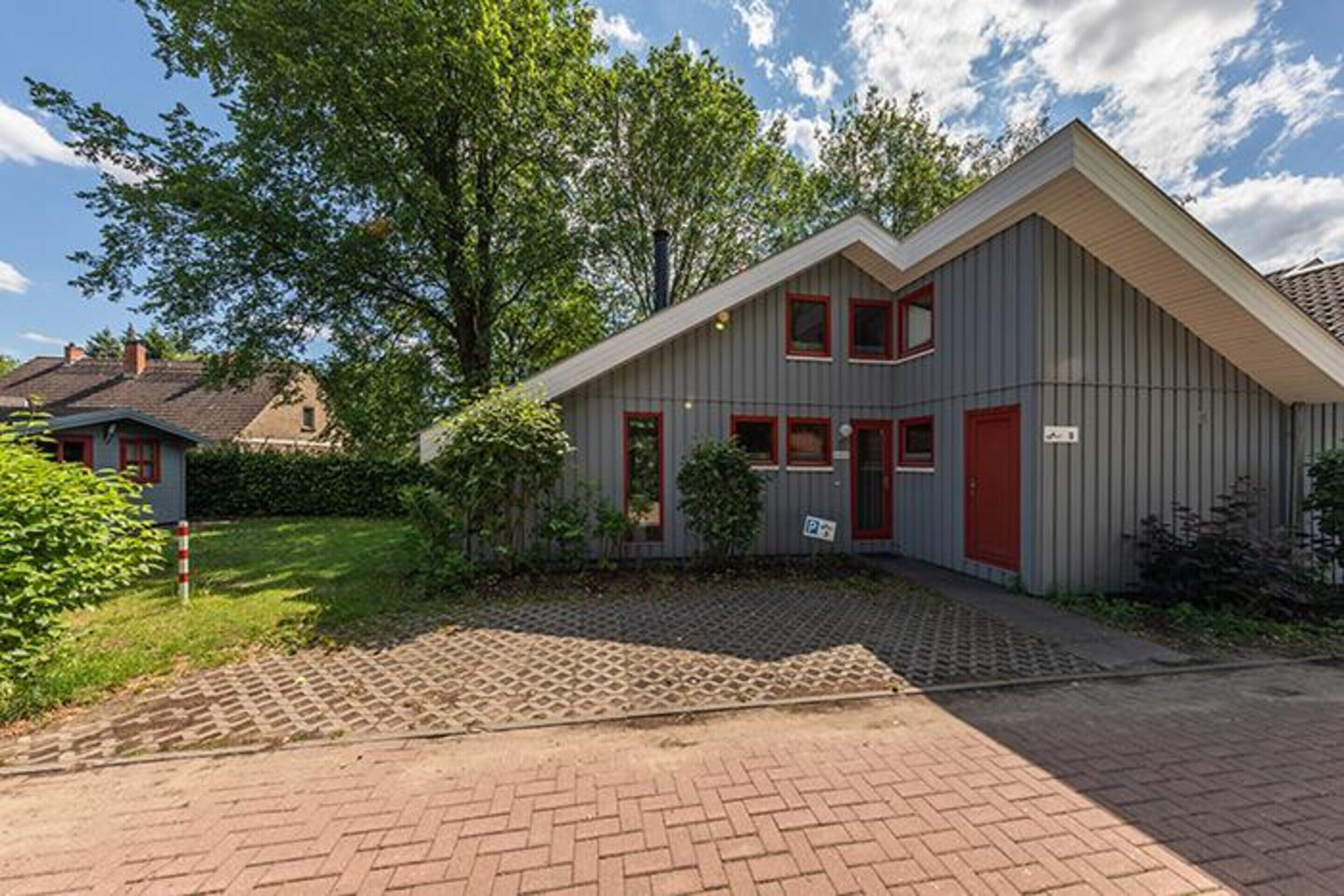 A single-story house with a grey exterior and red accents, a paved driveway, and a well-maintained garden.