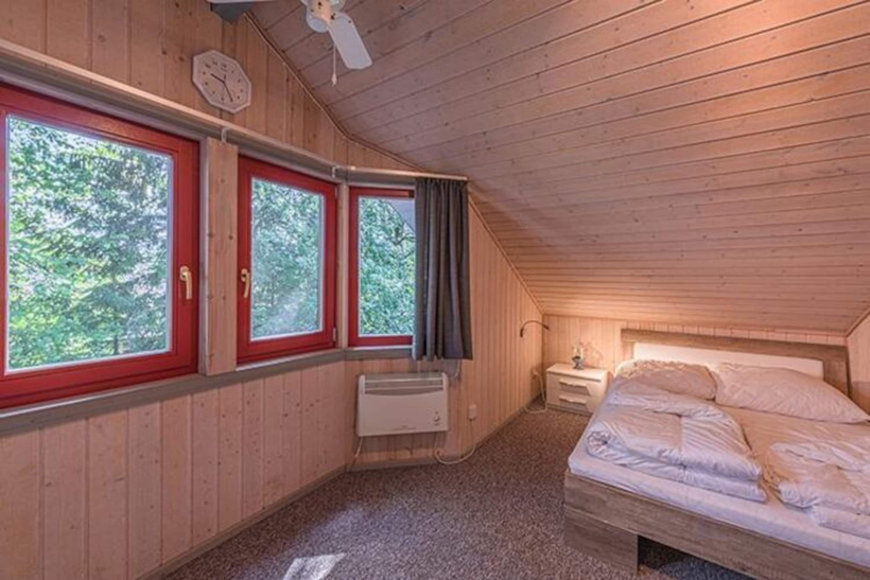 Une cabane avec un intérieur en bois, un lit, un chauffage et des fenêtres avec des rideaux.