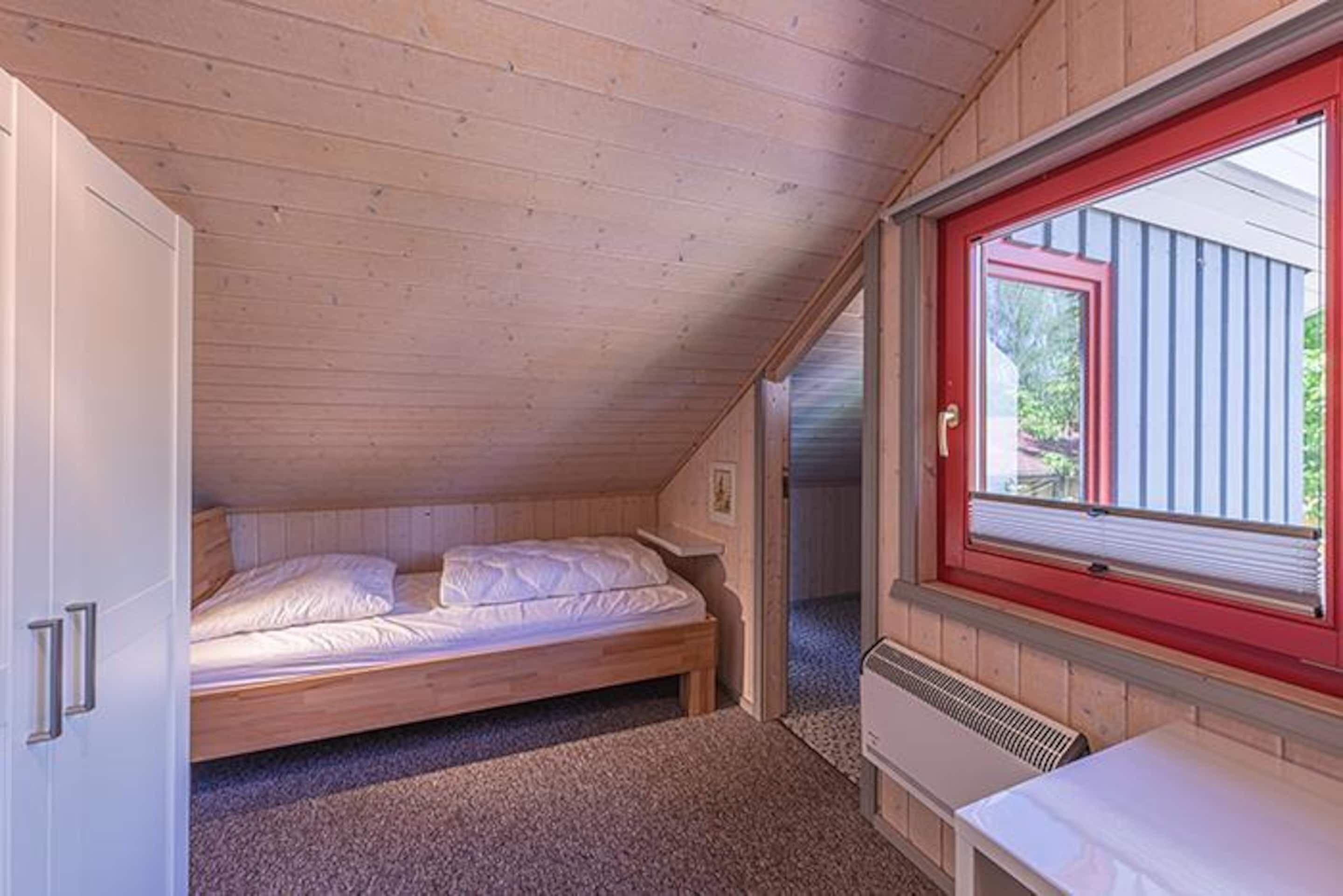 A small, single-bed room with wooden walls and a sloped ceiling.