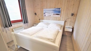Una stanza con rivestimento in legno, un letto, un quadro raffigurante una barca e una finestra con tende.