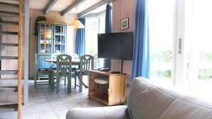 A cozy living room with a sofa, a TV, a wooden cabinet, and a dining area with chairs and a table. - Skandinavisches Ferienhaus in Mirow (Mirow)