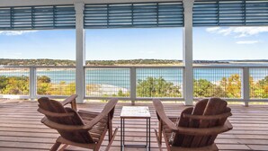 Une terrasse couverte, agrémentée de deux fauteuils Adirondack et d’une petite table, d’où l’on peut admirer un plan d’eau et une côte lointaine.