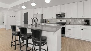 Une cuisine moderne avec des meubles blancs, un grand îlot central doté de tabourets, des appareils en acier inoxydable et un éclairage suspendu.
