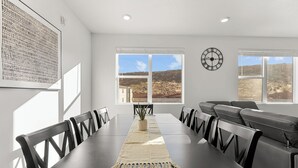Un espace de restauration moderne avec une longue table, des chaises, un arrangement floral en guise de centre de table et une vue sur un paysage désertique grâce à de grandes fenêtres.