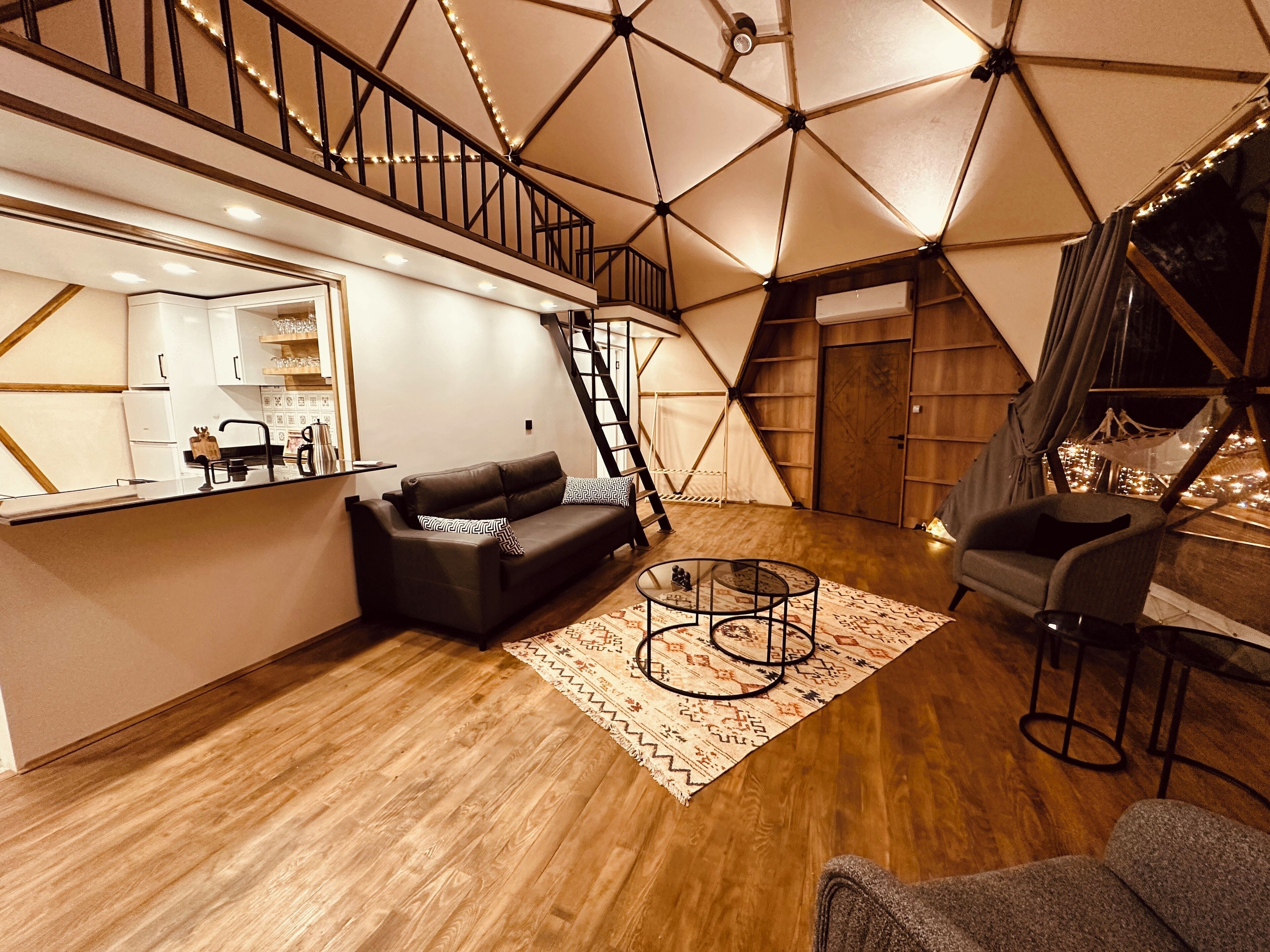 A modern living room with a geometric ceiling design, a black leather sofa, a coffee table, and a staircase leading to an upper level.