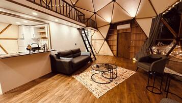 A modern living room with a geometric ceiling design, a black leather sofa, a coffee table, and a staircase leading to an upper level.