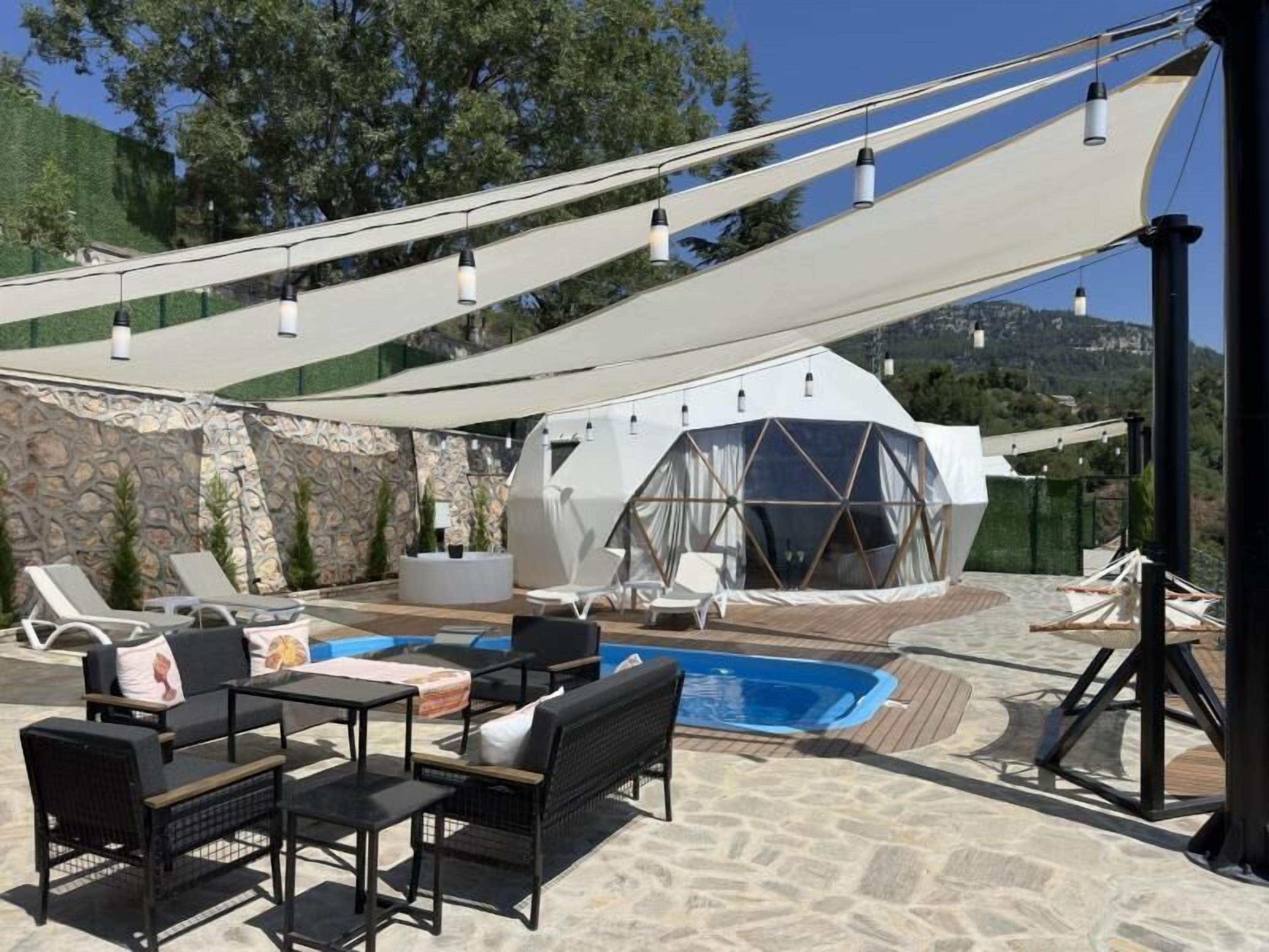 Un espace extérieur aménagé avec des fauteuils et des tables, une piscine et une structure en forme de dôme géodésique.