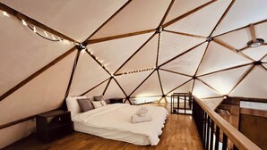 Een kamer in driehoekige vorm met een bed, houten vloer en een leuning.