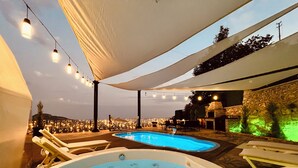 Een zwembadterras met twee jacuzzi's, sfeerverlichting en een stenen muur.