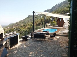 An outdoor patio with a stone floor, a swimming pool, and a barbecue area.