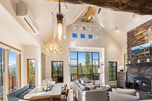 A spacious living room with a fireplace, large windows, and a view of mountains. - Big Sky Vacation Rentals: MMH 7 Derringer (Big Sky)