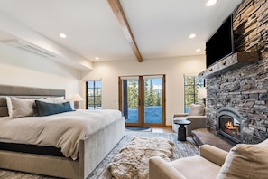 A bedroom with a large bed, a stone fireplace, and a view of the outdoors. - Big Sky Vacation Rentals: MMH 7 Derringer (Big Sky)