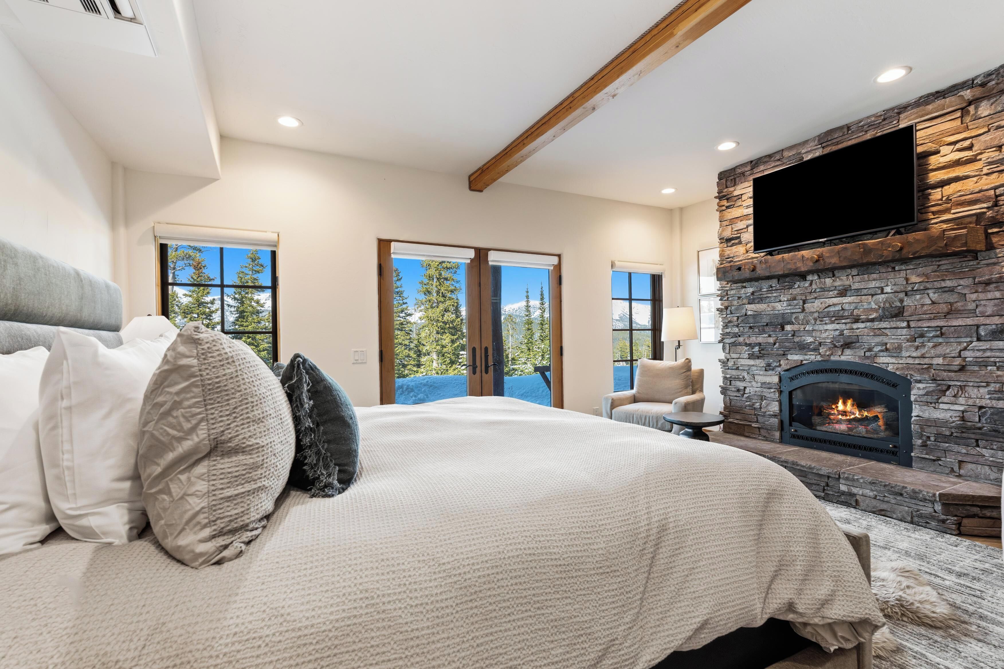 A bedroom with a large bed, a stone fireplace, and a television mounted on the wall.