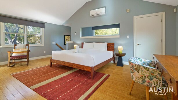 A bedroom with a bed, a chair, a nightstand, a window, and an air conditioning unit.