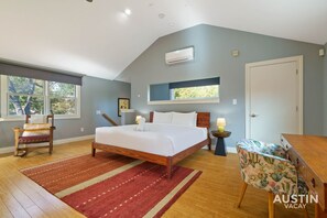 A bedroom with a bed, a chair, a nightstand, a window, and an air conditioning unit.