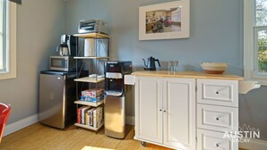 A compact kitchen with a refrigerator, microwave, coffee maker, and a small coffee table with a bowl and salt shakers.