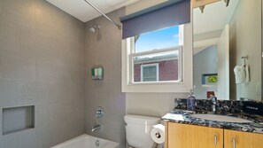 A bathroom with a bathtub, toilet, and vanity with a mirror.