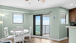 A dining area with a table and chairs, a view of the ocean through a sliding door, and a kitchen area with cabinets and a countertop. - T1811 at the Myrtle Beach Resort (Myrtle Beach)