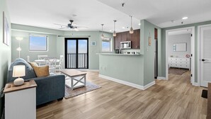 A modern living room with a sofa, coffee table, and a dining area with chairs. There is a kitchen with a microwave and a refrigerator. The room has a ceiling fan and pendant lights. - T1811 at the Myrtle Beach Resort (Myrtle Beach)